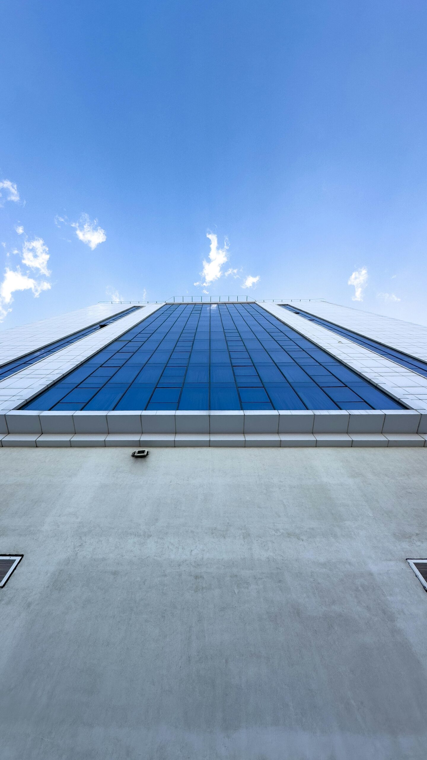 Architectural perspective of a glass skyscraper against a bright blue sky.
